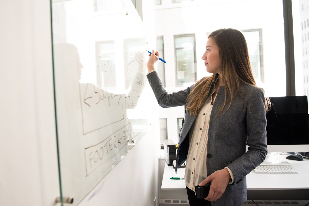 Offerings Professional woman writing on a whiteboard in an office environment, focusing on ideas.